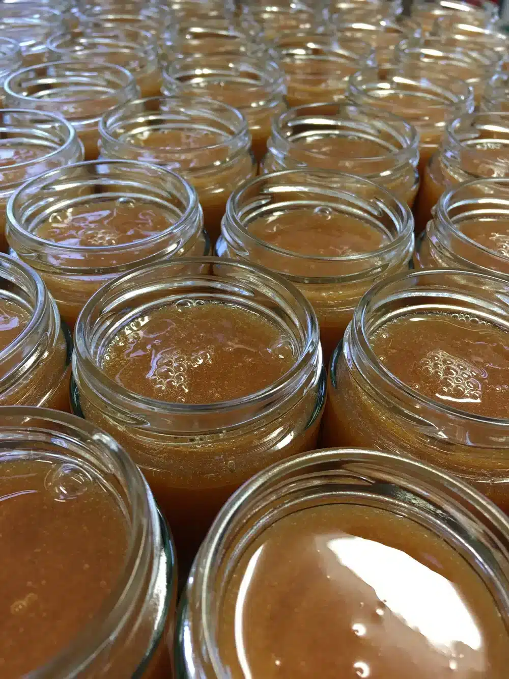 Rows of open glass jars filled with heather honey, arranged closely together, showing the smooth golden-brown texture and subtle bubbles on top. Perfect for your subscription: 2 jars delivered every 3 months.