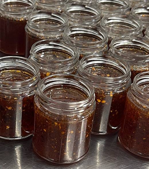 Several open glass jars filled with a chunky, dark brown sauce or condiment are arranged closely together on a reflective surface.